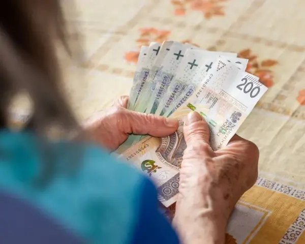 Dłonie starszej osoby liczą banknoty 200 zł. Może to symbolizować drugą waloryzację emerytur i wzrost dochodów.