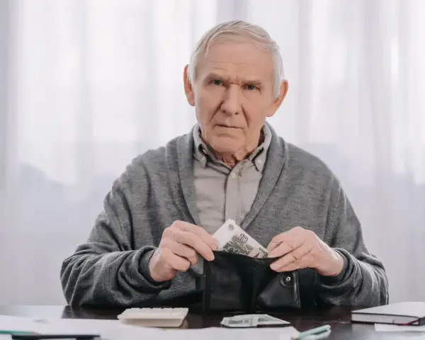 Zmartwiony starszy mężczyzna wkłada pieniądze do portfela, planując wcześniejszą emeryturę.