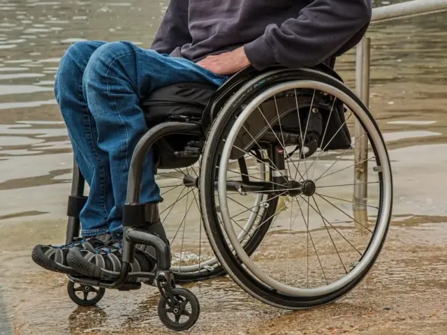 Osoba na wózku inwalidzkim, oczekująca na zus świadczenie wspierające, siedzi przy wodzie.