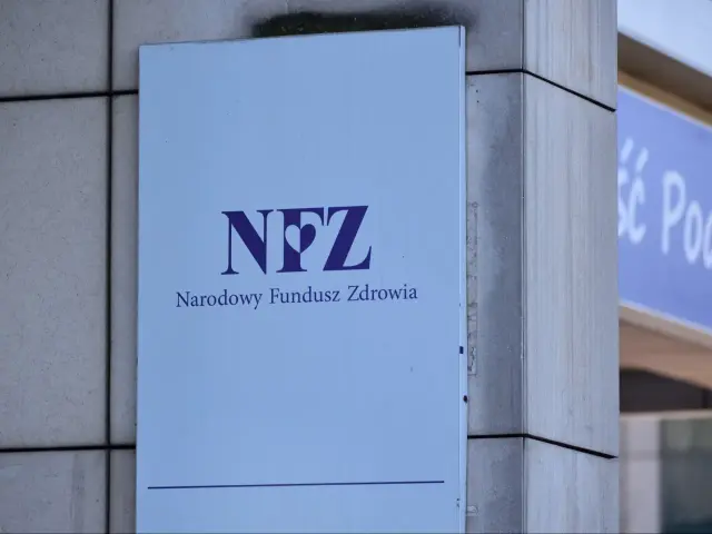 Tablica z logo NFZ (Narodowy Fundusz Zdrowia) i napisem "Narodowy Fundusz Zdrowia". Zapewnia dostęp do ubezpieczenia zdrowotnego.