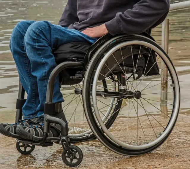 Osoba na wózku inwalidzkim, oczekująca na zus świadczenie wspierające, siedzi przy wodzie.