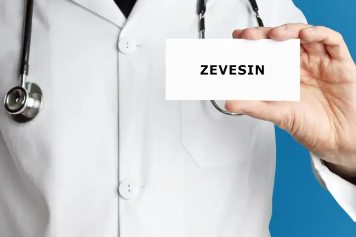 Lekarz w białym kitlu trzyma kartkę z napisem ZEVEISIN. Stetoskop wisi na jego szyi.