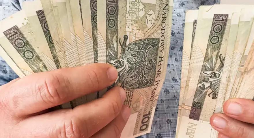 Ręce trzymające stos banknotów 100 zł. Zastanawiasz się, kiedy najlepiej przejść na emeryturę w 2026 roku?
