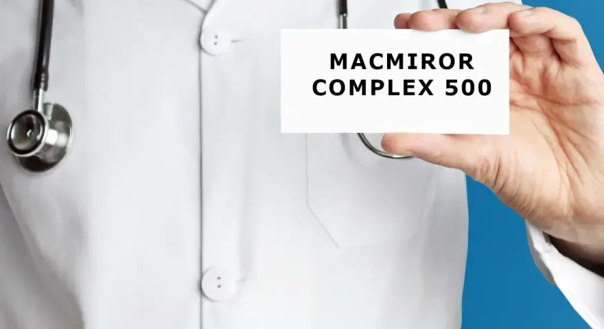 Lekarz w białym kitlu trzyma kartkę z napisem MACMIROR COMPLEX 500. Stetoskop wisi na jego szyi.