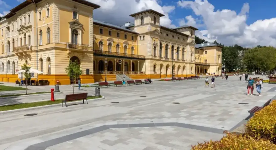 Plac przed sanatorium, gdzie obowiązują nowe zasady wyjazdu do sanatorium na NFZ. Ludzie spacerują po nowoczesnym deptaku.