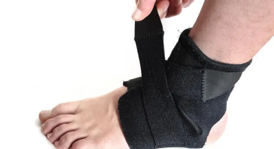 Dłoń zapina czarną ortezę na stopę, zapewniając wsparcie i stabilizację.