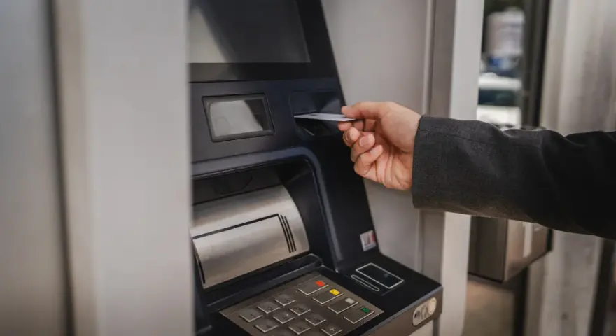 Dłoń wsuwa kartę do bankomatu, by sprawdzić, ile można wypłacić.