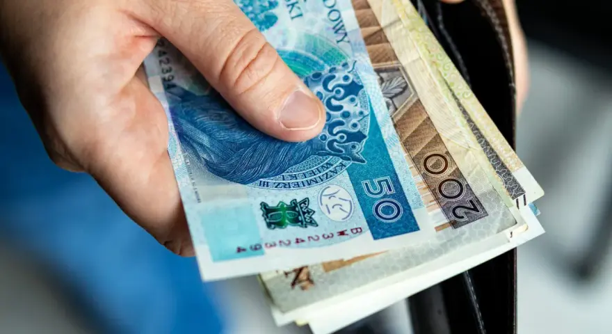 Dłoń trzyma polskie banknoty 50 i 200 zł. Zastanawiasz się nad nowymi zasadami przejścia na emeryturę? Tabela z wyliczeniami pomoże!