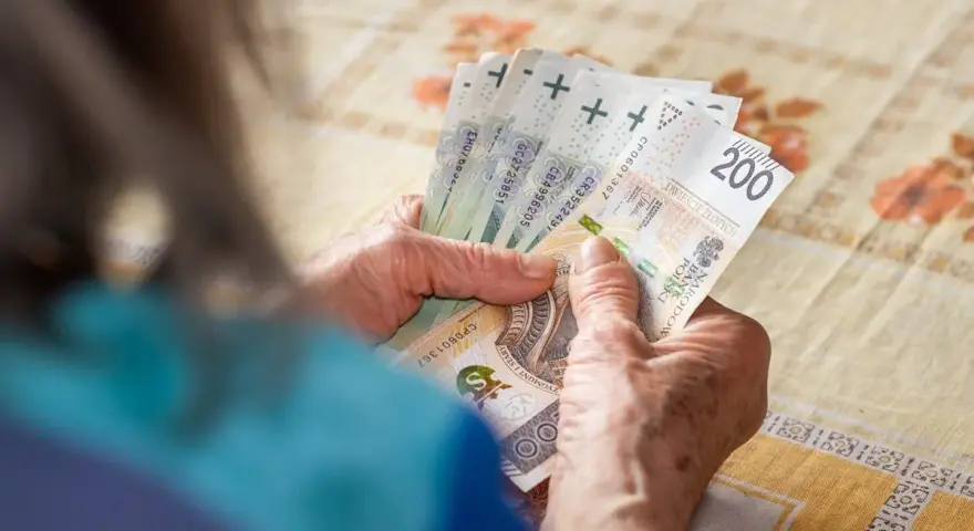 Dłonie starszej osoby liczą banknoty 200 zł. Tabela 13 emerytura 2026 może zawierać podobne kwoty.