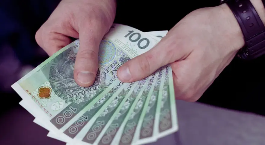 Dłonie trzymają stos banknotów 100 zł. Czy to wystarczy, by pokryć ile wynosi najniższa krajowa?