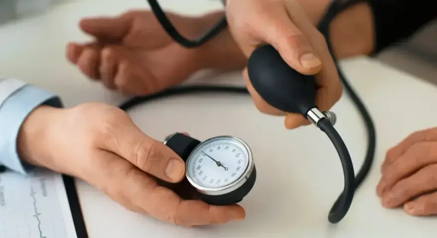 Lekarz mierzy ciśnienie krwi pacjentowi. Na stole leży ciśnieniomierz, a obok dokument z zapisem EKG. To ważny element profilaktyki, dbanie o prenessa jest kluczowe.