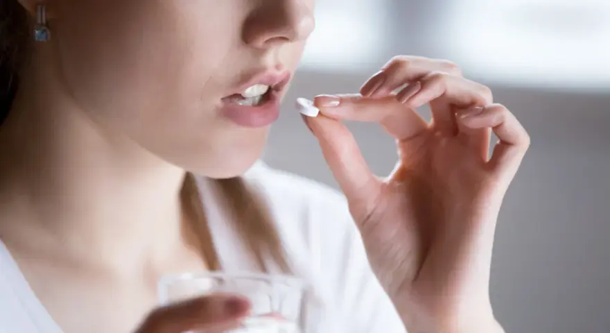 Kobieta bierze tabletkę clindamycin mip 600, trzymając szklankę wody.