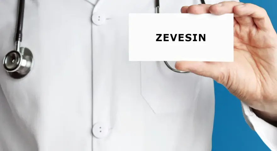 Lekarz w białym kitlu trzyma kartkę z napisem ZEVEISIN. Stetoskop wisi na jego szyi.