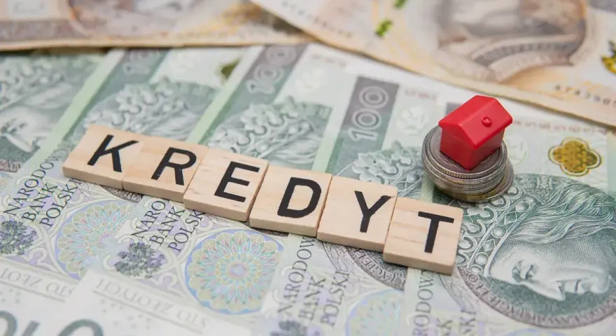 Litery układające słowo "KREDYT" na banknotach. Mały czerwony domek na stosie monet symbolizuje pomoc w spłacie kredytu, np. z funduszu wsparcia kredytobiorców.