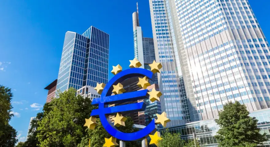 Symbol euro przed nowoczesnymi wieżowcami, siedziba europejskiego banku centralnego.