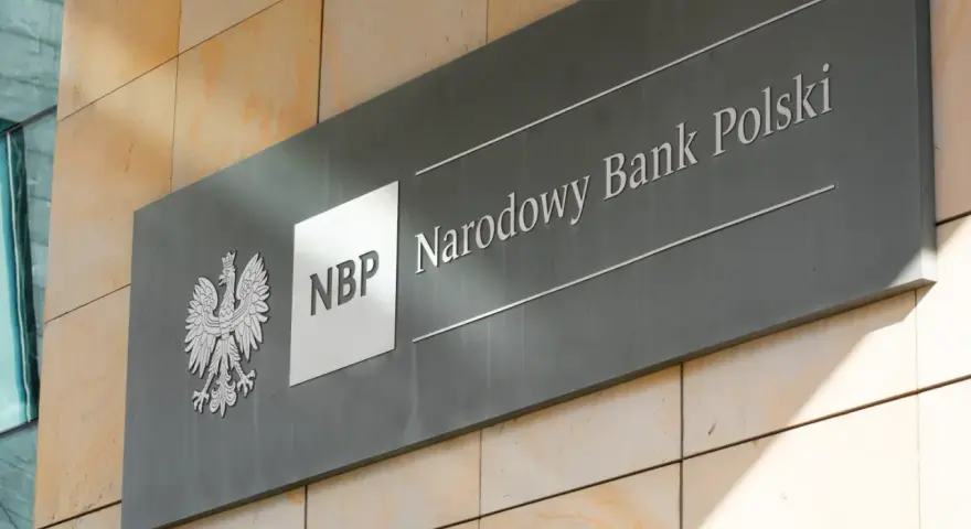 Tablica z godłem Polski i napisem "NBP Narodowy Bank Polski". Decyzje NBP wpływają na obniżkę stopy procentowej.