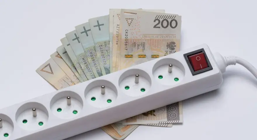Pieniądze leżą pod listwą z gniazdkami, symbolizując zamrożenie cen prądu.