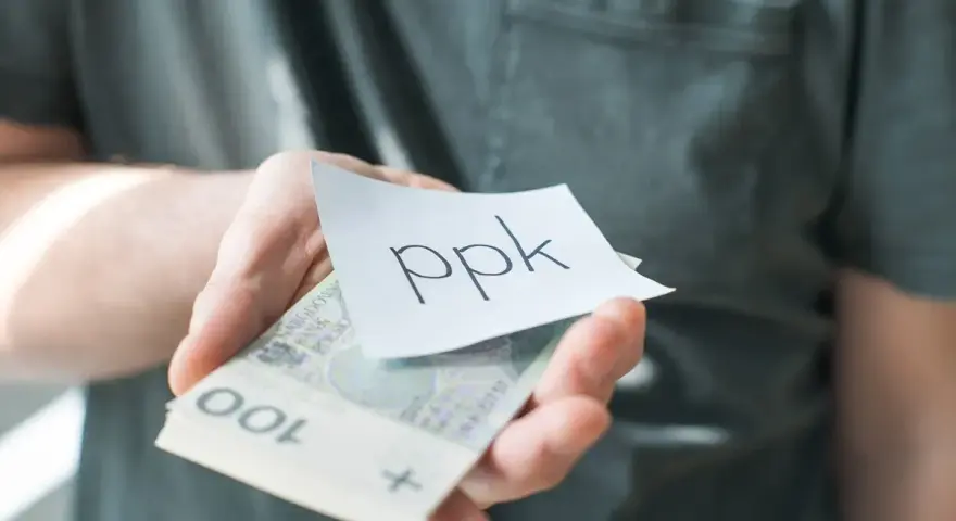 Dłoń trzyma banknoty i karteczkę z napisem "ppk". Jak sprawdzić swoje oszczędności?