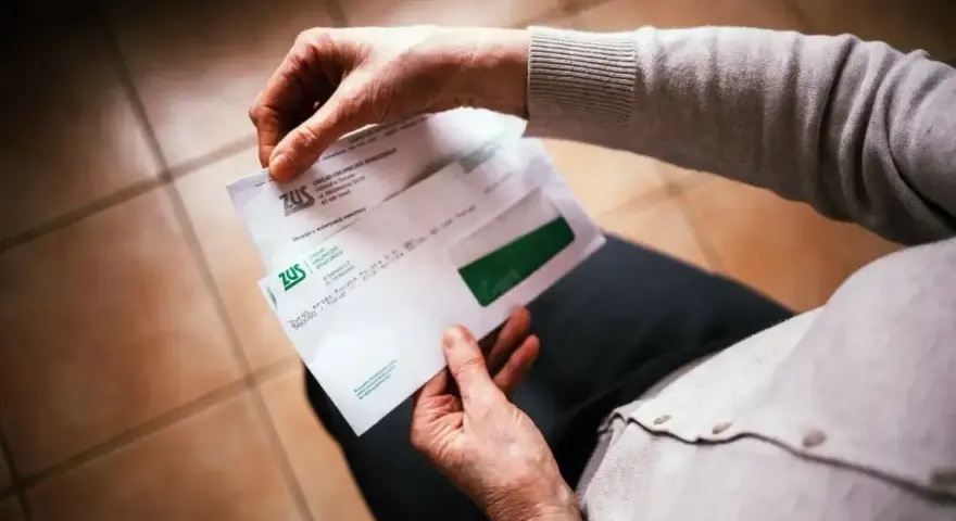 Dłonie trzymają kopertę ZUS. W środku dokumenty dotyczące 13 emerytury netto.
