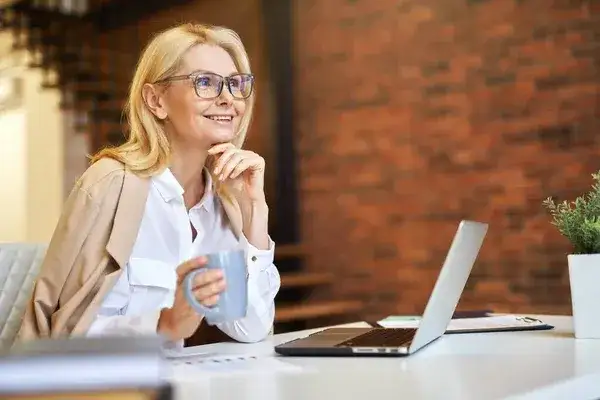 Dojrzała kobieta na laptopie, uśmiechnięta, w biurze