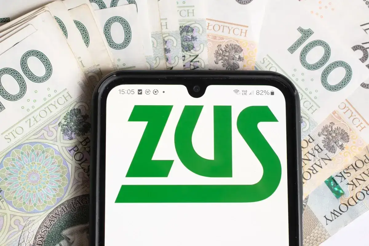 ZUS na ekranie telefonu, obok banknotów 100 zł. Sprawdzasz, renta alkoholowa ile wynosi?