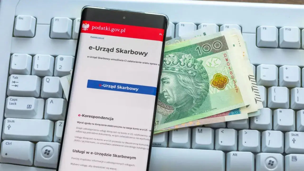 Na klawiaturze leży smartfon z aplikacją e-Urząd Skarbowy i polskie banknoty. Możliwe, że to przygotowanie do rozliczenia ulgi rehabilitacyjnej na samochód.