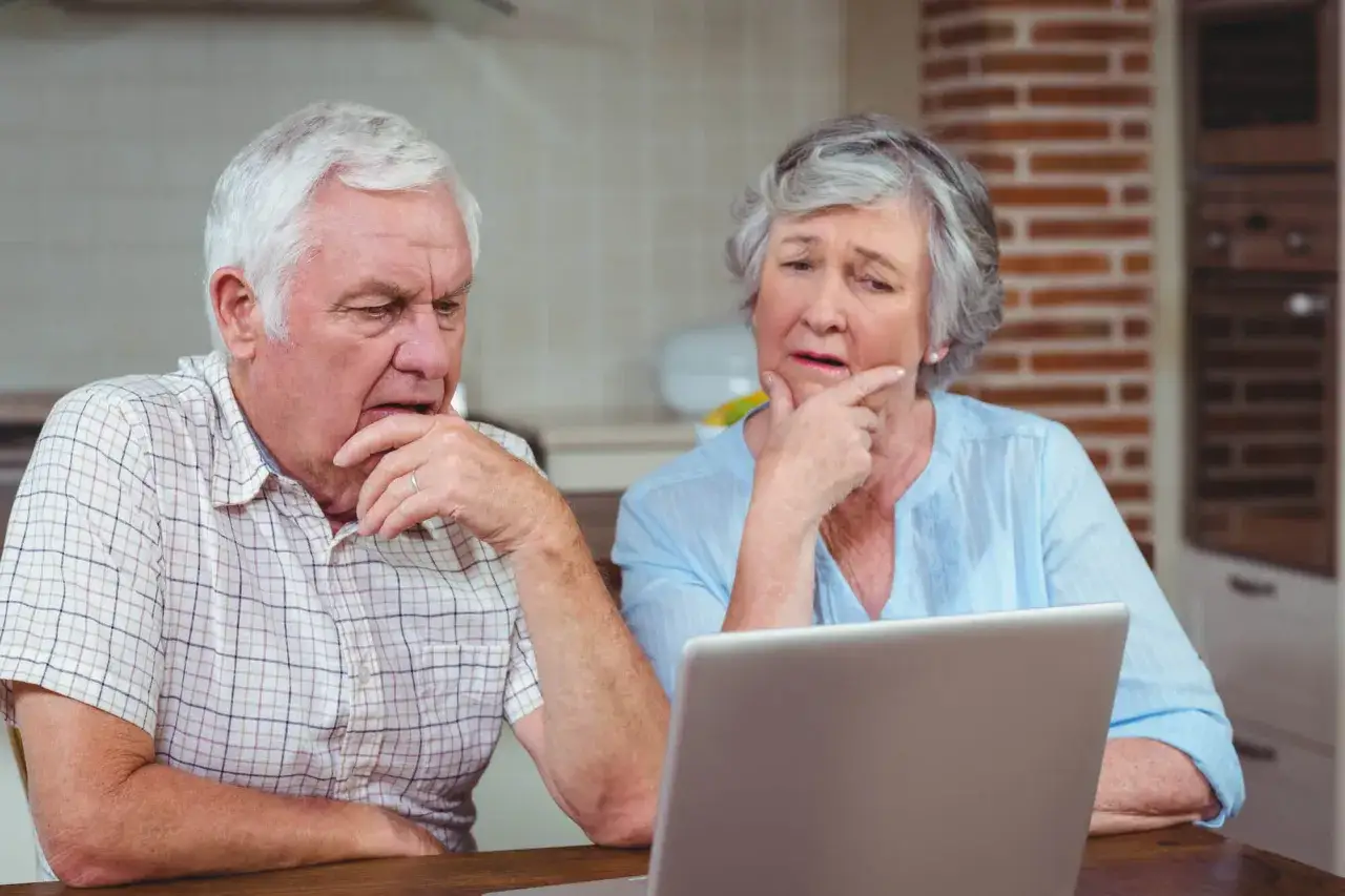 Zastanawiają się, dla kogo jest bon senioralny. Para seniorów z zamyśloną miną patrzy na ekran laptopa.