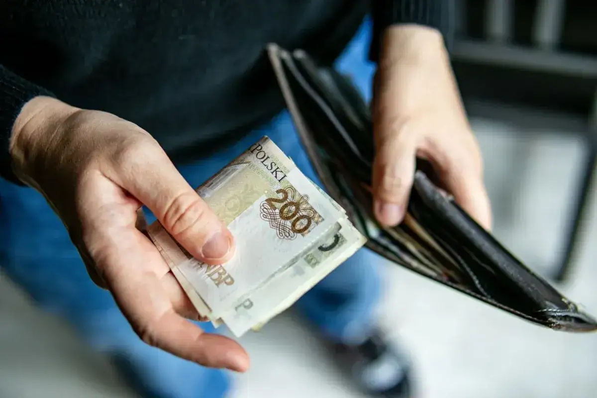 Dłonie trzymają polskie banknoty 200 zł i pusty portfel. Czy to zapowiedź świadczenia pielęgnacyjnego 2026?