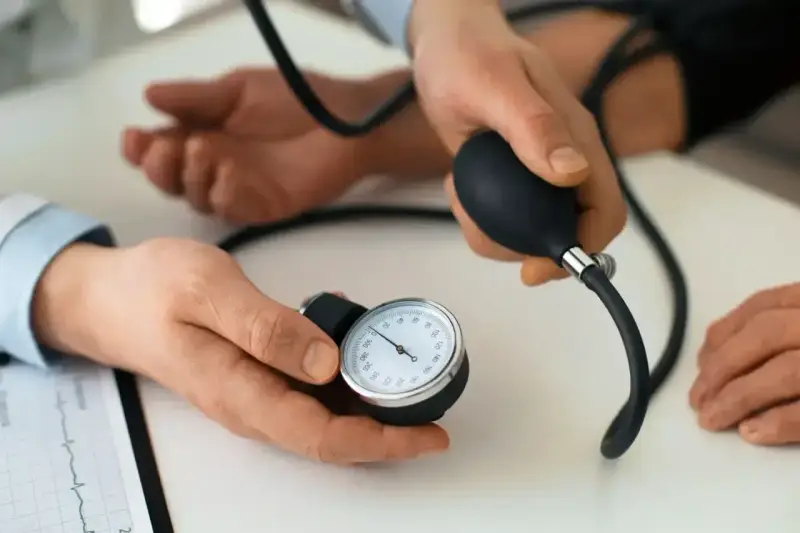 Lekarz mierzy ciśnienie krwi pacjentowi. Na stole leży ciśnieniomierz, a obok dokument z zapisem EKG. To ważny element profilaktyki, dbanie o prenessa jest kluczowe.